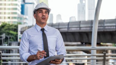 Üst düzey Amerikan inşaat mühendisi hard kasketli, modern şehrin kağıt planı üzerine notlar alıyor. Mühendislik araştırması ya da şehirdeki inşaat alanındaki gelişmeleri kontrol etmek.