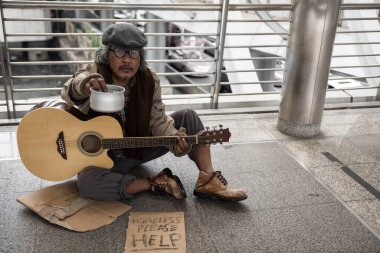 Yaşlı dilenci ya da evsiz pis adam bağış kasesi tutarak bağış istemek için gitar ve kağıt kartonla bağış istemek. Şehirdeki yoksulluk