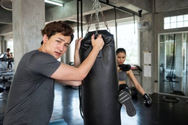 Asyalı bayan boksör fitness salonunda tekme atarken kişisel antrenörün portresi boks kum torbası tutuyor. Atletik kadın vücut geliştirme ve sağlıklı yaşam tarzı konsepti için koçla boks yapıyor..