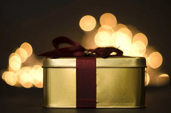 Golden Christmas gift box with a red ribbon on background of defocused golden lights.