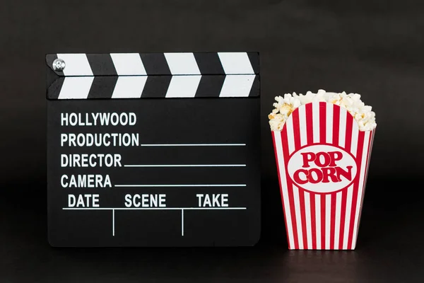 Clapboard and classic popcorn box on black background