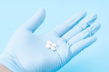 Mavi eldivenli el mavi arka planda farklı haplar tutuyor.