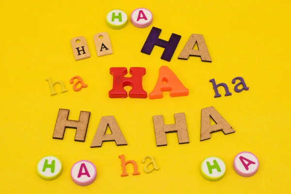 Ha, ha, ha, laugh made with letters of different colors, sizes and materials on yellow background