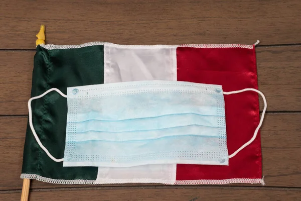 Face mask and Mexican or Italian flag on wooden background