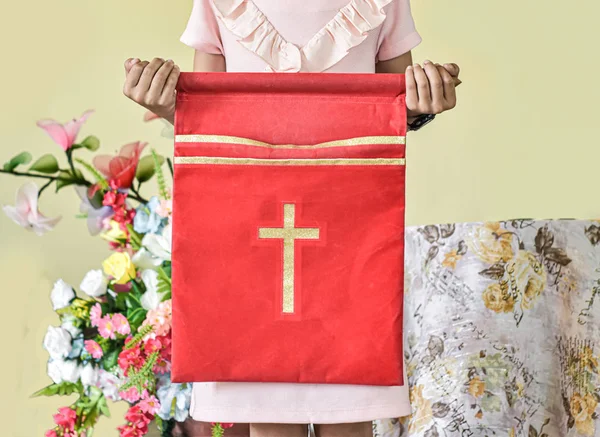 Children\'s hand holding velvet offering bag used in church.