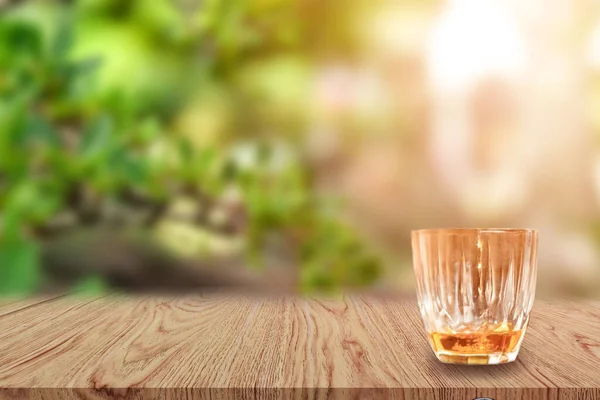 A glass of Whiskey on wooden table and light blurred nature background.
