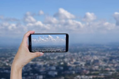 Fotoğraf çekmek için el ele tutuşan akıllı telefon bir bulut ve şehir.