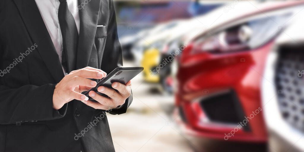 Businessman using smartphone on blurred background of new car displayed in showroom dealer with copy space.