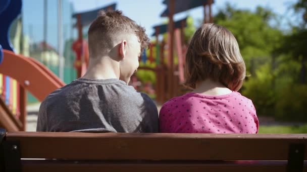 Хлопчик і дівчинка сидять на лавці — стокове відео