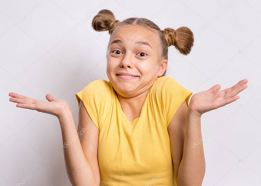 Teen girl showing helpless gesture with hands - I do not know. Cute young teenager in yellow t-shirt, on grey background. Shrugging, confused child making helpless sign and looking at camera.