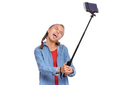Sopayla selfie yapan mutlu genç kız portresi. Akıllı telefona poz veren ergen, suratını buruşturan, beyaz arka planda soyutlanmış komik bir yüz. Sosyal ağ için cep telefonundan selfie çeken çocuk.
