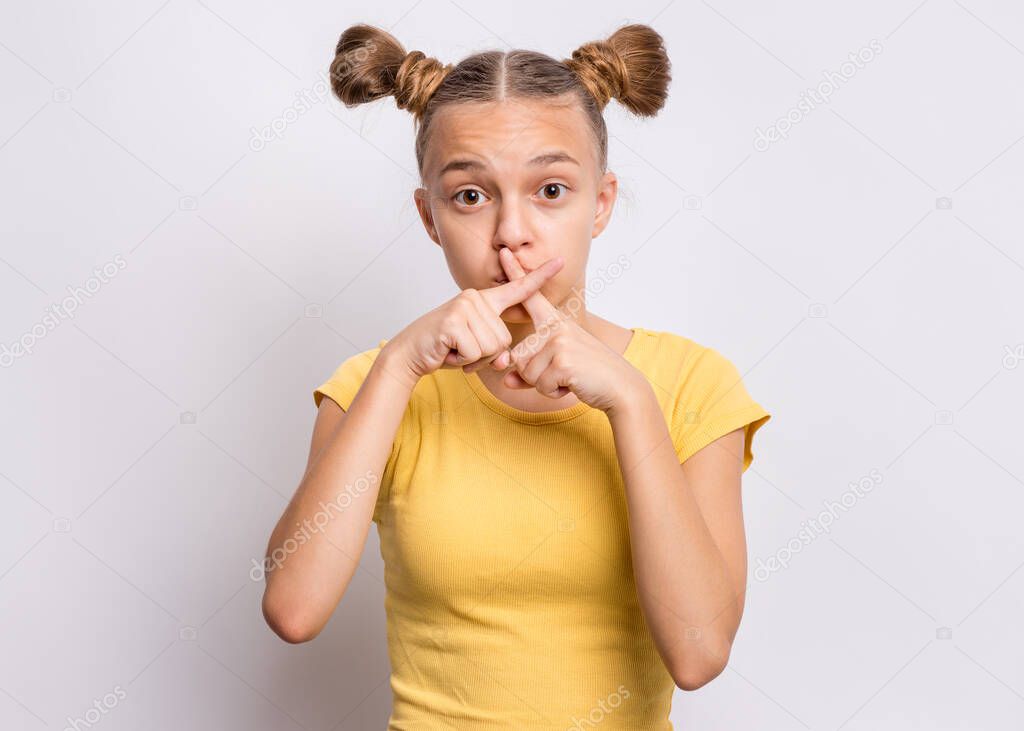 Portrait of teen girl asking to be quiet with fingers on lips, isolated on white background. Beautiful young teenager making keep Quiet gesture - covers her mouth. Speak no evil concept.