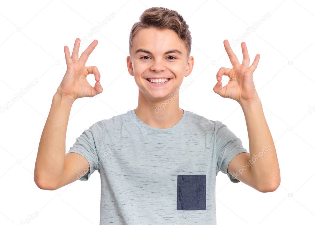 Portrait of teen boy making Ok gesture, isolated on white background. Handsome caucasian young teenager smiling and giving OK sign. Happy cute child showing okay.