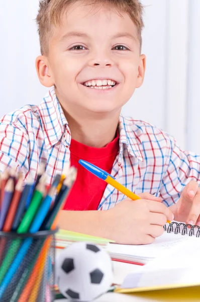 在餐桌边做家庭作业的青春期男孩笑着 小男孩坐在教室的书桌前 又回到了学校的概念 — 图库照片