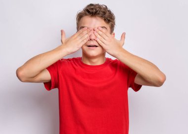 Gülümseyen bir gencin portresi. Elleri yüzün üzerinde, gözleri sürpriz olsun diye kapatıyor. Avuç içleriyle güzel, güzel, kapalı gözler. Gri arka planda mutlu beyaz çocuk. Şeytani bir kavram değil.