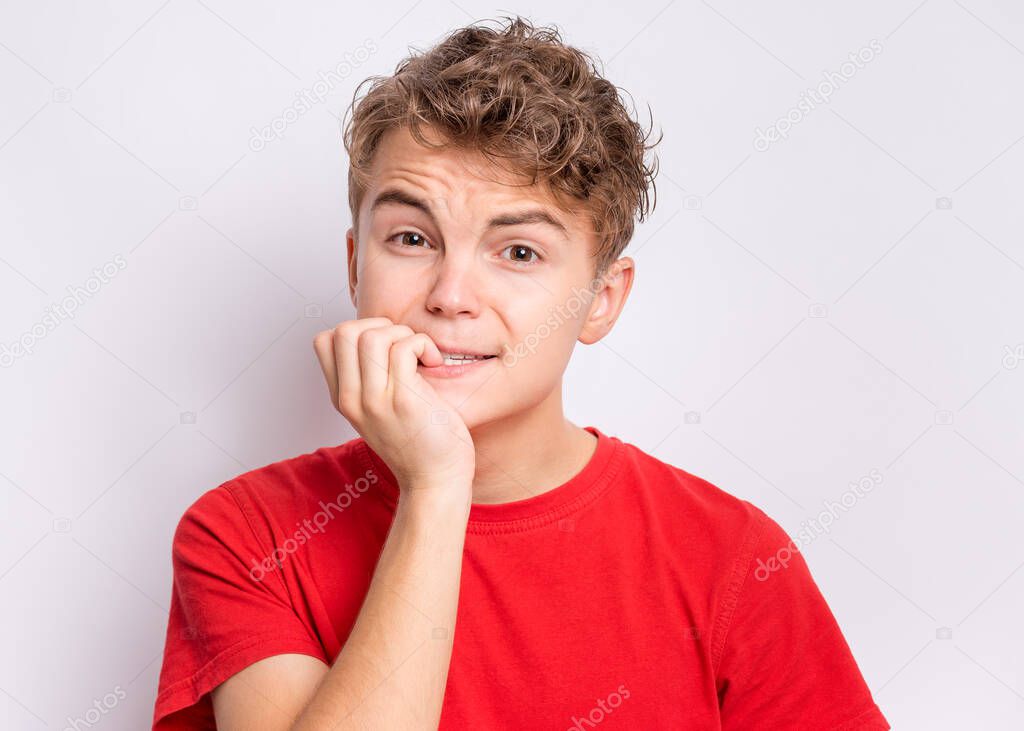 Portrait of unhappy teen boy looking stressed and nervous with hands on mouth biting nails. Funny guy something very frightened. Child gnaws his nails for fear, afraid of punishment.