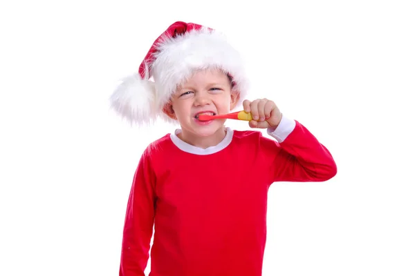 Noel dişçiliği. Kırmızı Noel Baba kostümlü ve beyaz arka planda diş fırçalayan mutlu sarışın çocuk. Sağlık hizmeti, diş hijyeni konsepti. Model, boş alan.