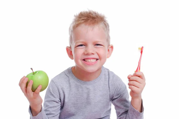 Niño rubio feliz sonriendo con manzana verde y cepillo de dientes sobre fondo blanco. Cuidado de la salud, higiene dental, cepillado de dientes concepto. Burla, espacio libre —  Fotos de Stock