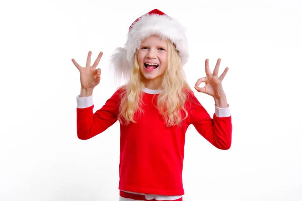 Det avtalet håller jag med om. Spännande glad liten flicka i röd jul Santa hatt leende och visar okej ok, inga problem tecken, ge positiv feedback, liksom idé, att bedöma cool produkt. På vitt. — Stockfoto