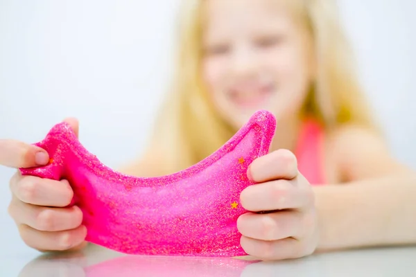Menina loira esticando rosa brilho lodo para os lados. Crianças mãos jogando brinquedo lodo. A fazer lodo. Espaço de cópia. Foco seletivo. — Fotografia de Stock
