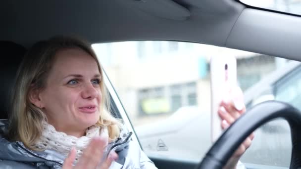 Mujer joven blogger en ropa de invierno sentada en coche y hablando con sus seguidores, transmisión en vivo, mirando a la pantalla del teléfono inteligente. Redes sociales, instagram, video chat y concepto de tecnología — Vídeo de stock