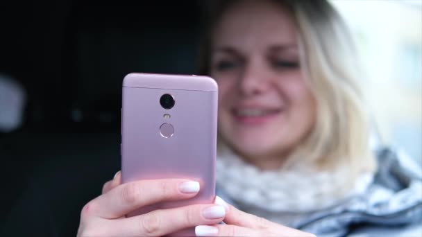 Wazig blonde vrouw blogger in de winter kleren zitten in de auto en praten met volgers, live streaming, op zoek naar smartphone scherm. focus op telefoon. — Stockvideo