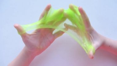 Yanlara yeşil balçık geren bir kız. Çocuk elleri sümük oyuncağı oynuyor. Beyazdan balçık yapmak. Modaya uygun sıvı oyuncak ellere ve parmaklara yapışıyor. 4k görüntü