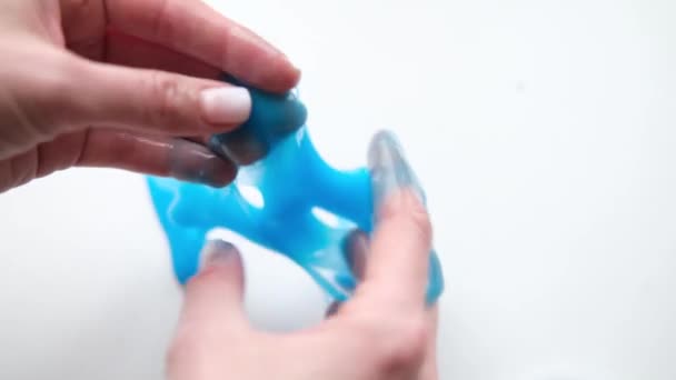 Menina esticando lodo azul para os lados. Mãos de mulher brincando de brinquedo viscoso. A fazer lodo no branco. Brinquedo líquido na moda adere a mãos e dedos. Filmagem 4k — Vídeo de Stock