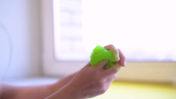 Dziewczyna rozciąga zielony szlam na boki. Dzieciaki bawią się w szlamową zabawkę. Robi szlam na białym. Modna płynna zabawka przykleja się do rąk i palców. Materiał 4k — Wideo stockowe