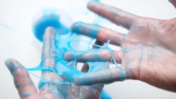 女孩把蓝色的黏液伸向两边. 女人的手在玩泥巴玩具。 使黏液在白色上。 时髦的液体玩具粘在手和手指上. 4k镜头 — 图库视频影像