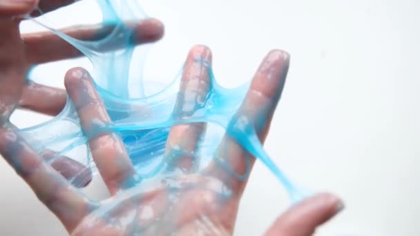 Menina esticando lodo azul para os lados. Mãos de mulher brincando de brinquedo viscoso. A fazer lodo no branco. Brinquedo líquido na moda adere a mãos e dedos. Filmagem 4k — Vídeo de Stock