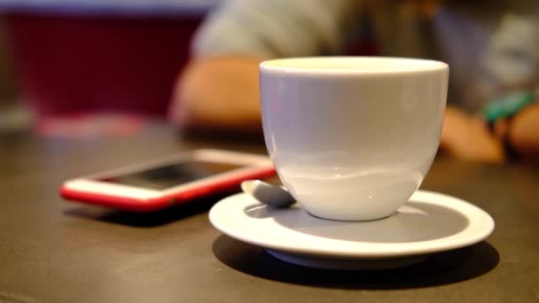 Café. Mujer recortada toma el teléfono rojo, comprueba los mensajes mientras bebe café en el restaurante, cafetería. Primeros planos de las manos de las mujeres con copa blanca. Oscura escena tonificada cálida . — Vídeos de Stock