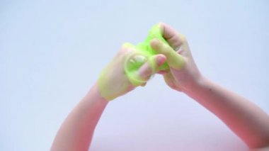 Yanlara yeşil balçık geren bir kız. Çocuk elleri sümük oyuncağı oynuyor. Beyazdan balçık yapmak. Modaya uygun sıvı oyuncak ellere ve parmaklara yapışıyor. 4k görüntü