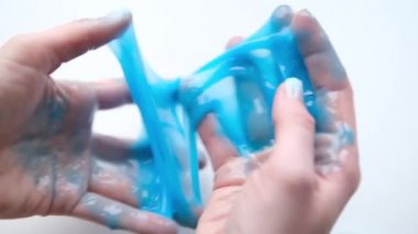 Yanlara mavi balçık geren bir kız. Kadın elleri balçık oyuncağı oynuyor. Beyazdan balçık yapmak. Modaya uygun sıvı oyuncak ellere ve parmaklara yapışıyor. 4k görüntü