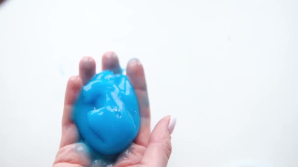 Menina esticando lodo azul para os lados. Mãos de mulher brincando de brinquedo viscoso. A fazer lodo no branco. Brinquedo líquido na moda adere a mãos e dedos. Filmagem 4k — Vídeo de Stock