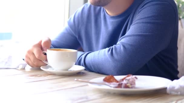 Café da manhã. Homem caucasiano em azul bebendo café ot chá no restaurante, café. Mãos de homem de close-up com copo branco . — Vídeo de Stock