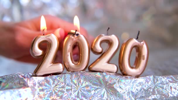 Γυναίκα ανάβει ένα φως κεριών 2020. Χρυσά κεριά καίγονται. Θολή ασημί φόντο. Καλά Χριστούγεννα και Καλή Χρονιά. Επιλεκτική εστίαση.Δημιουργική ζωντανή κάρτα χαιρετισμού. 4k πλάνα — Αρχείο Βίντεο