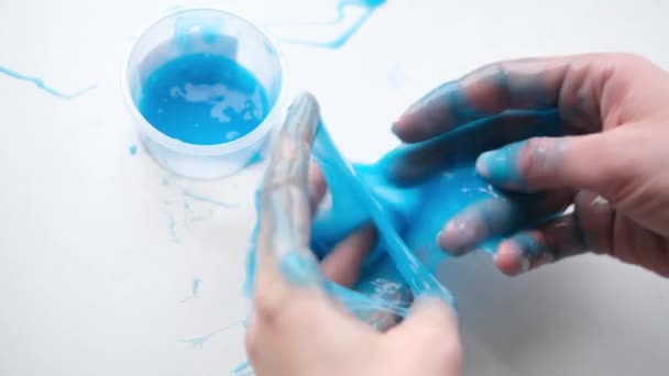 女孩把蓝色的黏液伸向两边. 女人的手在玩泥巴玩具。 使黏液在白色上。 时髦的液体玩具粘在手和手指上. 4k镜头 — 图库视频影像
