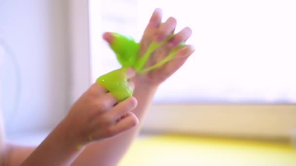 Ragazza che si estende bava verde ai lati. Le mani dei bambini che giocano al gioco della melma. Facendo melma su bianco. Il giocattolo liquido alla moda si attacca a mani e dita. 4k filmati — Video Stock