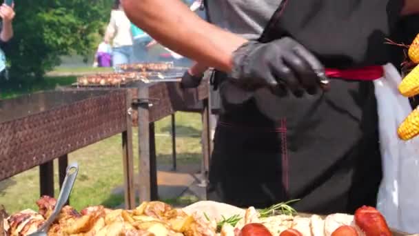 Streetfood-Festival. Ein Koch in schwarzer Kleidung und Handschuhen breitet gebratenes Essen auf Tellern aus. Kartoffeln, Grillwürste, Fleisch mit Spießen, Grillen. Lebensmittel aus nächster Nähe. — Stockvideo