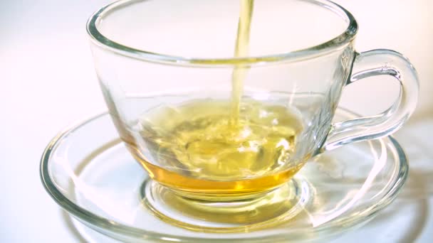 Verter té negro aromatizante de la tetera en una taza de té de vidrio transparente a juego sobre fondo blanco . — Vídeos de Stock