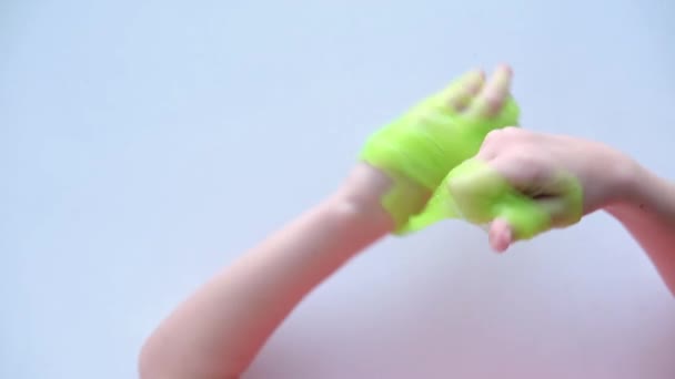 Ragazza che si estende bava verde ai lati. Le mani dei bambini che giocano al gioco della melma. Facendo melma su bianco. Il giocattolo liquido alla moda si attacca a mani e dita. 4k filmati — Video Stock