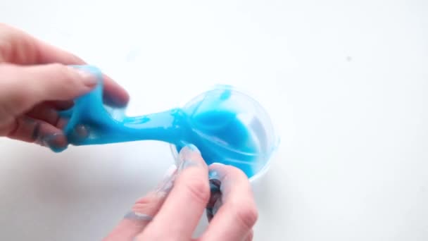 Menina esticando lodo azul para os lados. Mãos de mulher brincando de brinquedo viscoso. A fazer lodo no branco. Brinquedo líquido na moda adere a mãos e dedos. Filmagem 4k — Vídeo de Stock