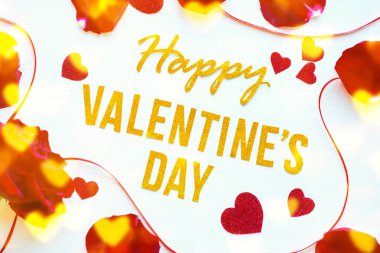 Sevgililer Günü 'nüz kutlu olsun. Kırmızı gül yaprakları ve beyaz tahta arka planda parlak kalpler olan altın yazılı tebrik kartı. romantik ve aşk konsepti