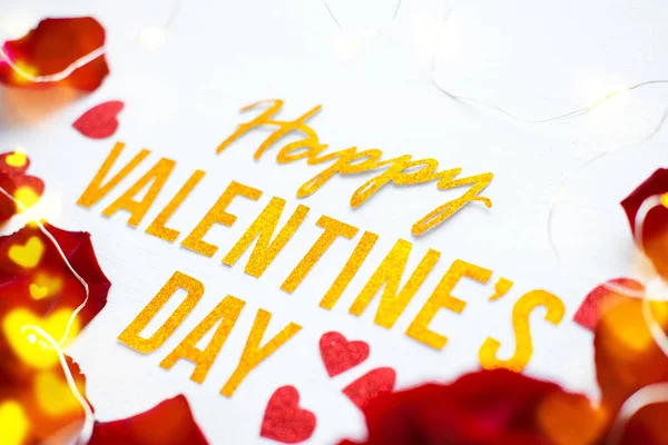 Поздравительная открытка на день святого Валентина с красными лепестками роз и сияющими сердцами на белом деревянном фоне. романтика и любовь — стоковое фото