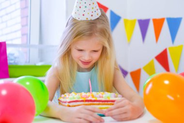 Sarışın beyaz kız rüyasında gülümsüyor ve gökkuşağı pastasına bakıyor. Balonlarla dolu renkli bir arka plan. Birhday partisi ve dilek konsepti