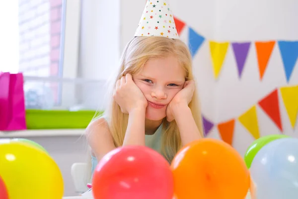 Chica caucásica rubia infeliz con cara aburrida cerca de pastel de arco iris de cumpleaños. Fondo colorido festivo. Mala fiesta de cumpleaños — Foto de Stock