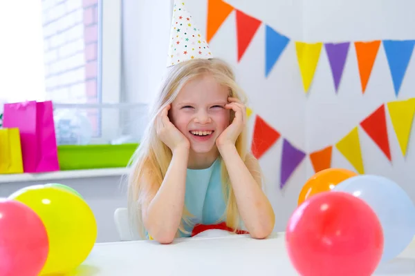 Retrato de chica rubia caucásica sonriendo en la fiesta de cumpleaños de la cámara. Fondo colorido festivo con globos. Foto vertical —  Fotos de Stock