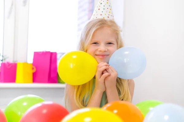 Retrato de chica rubia caucásica sonriendo en la fiesta de cumpleaños de la cámara. Fondo colorido festivo con globos. Foto vertical —  Fotos de Stock