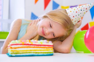 Sarışın beyaz kız rüyasında gökkuşağı pastasının yanında gülümsüyordu. Balonlarla şenlikli bir arkaplan
